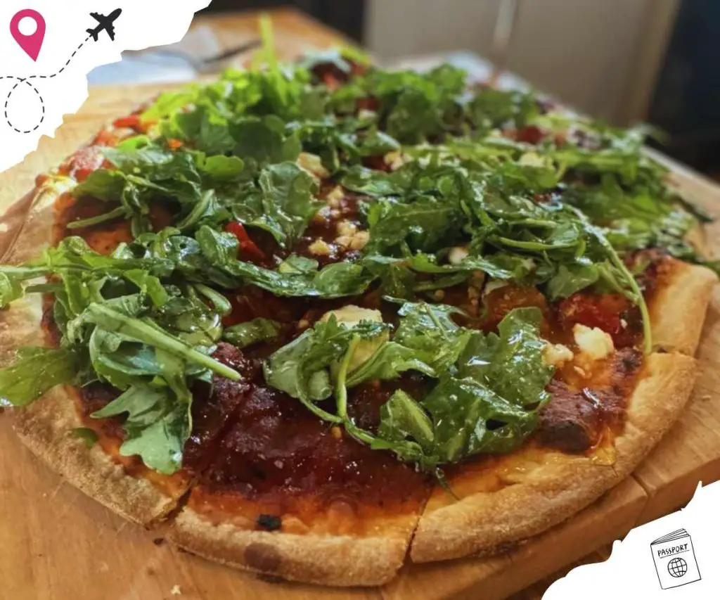 Fresh green salad toppings on a delicious homemade pizza, served on a wooden board, perfect for travel food enthusiasts and culinary explorers.