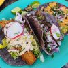 Fresh Mexican tacos with colorful toppings, radish slices, and lime on bright plate, showcasing authentic street food from a popular travel destination for culinary adventures.