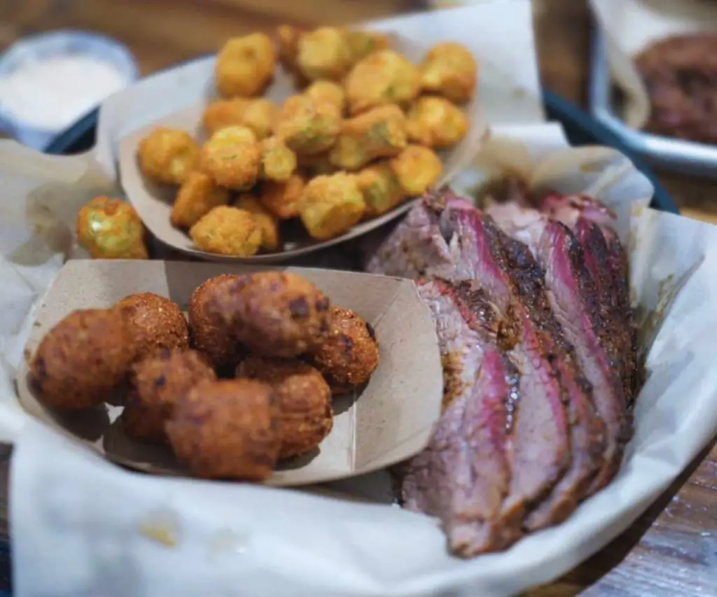 Crispy fried cauliflower bites, smoky brisket slices, and seasoned hush puppies served on a tray, showcasing classic Southern barbecue dishes. Perfect for a flavorful dining experience.