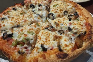 Cheese pizza with black olives, sausage, and green peppers on a golden crust at a pizzeria.