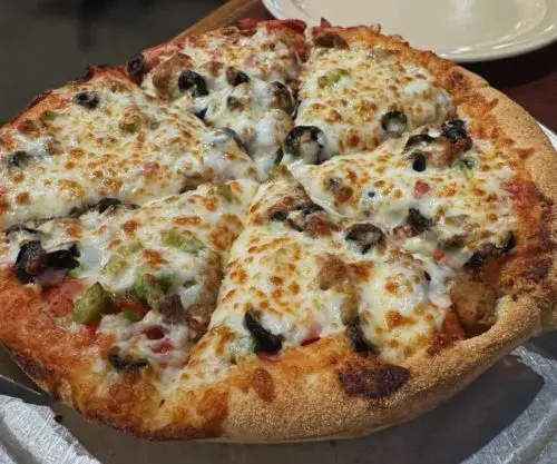 Cheese pizza with black olives, sausage, and green peppers on a golden crust at a pizzeria.