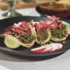 Fresh carne asada tacos on a black plate with lime wedges and radish slices, showcasing authentic Mexican street food and vibrant flavors.