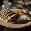 Crepe with chocolate and white syrup, served with Mexican chili and cheese on a plate in a restaurant setting.