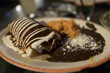 Crepe with chocolate and white syrup, served with Mexican chili and cheese on a plate in a restaurant setting.