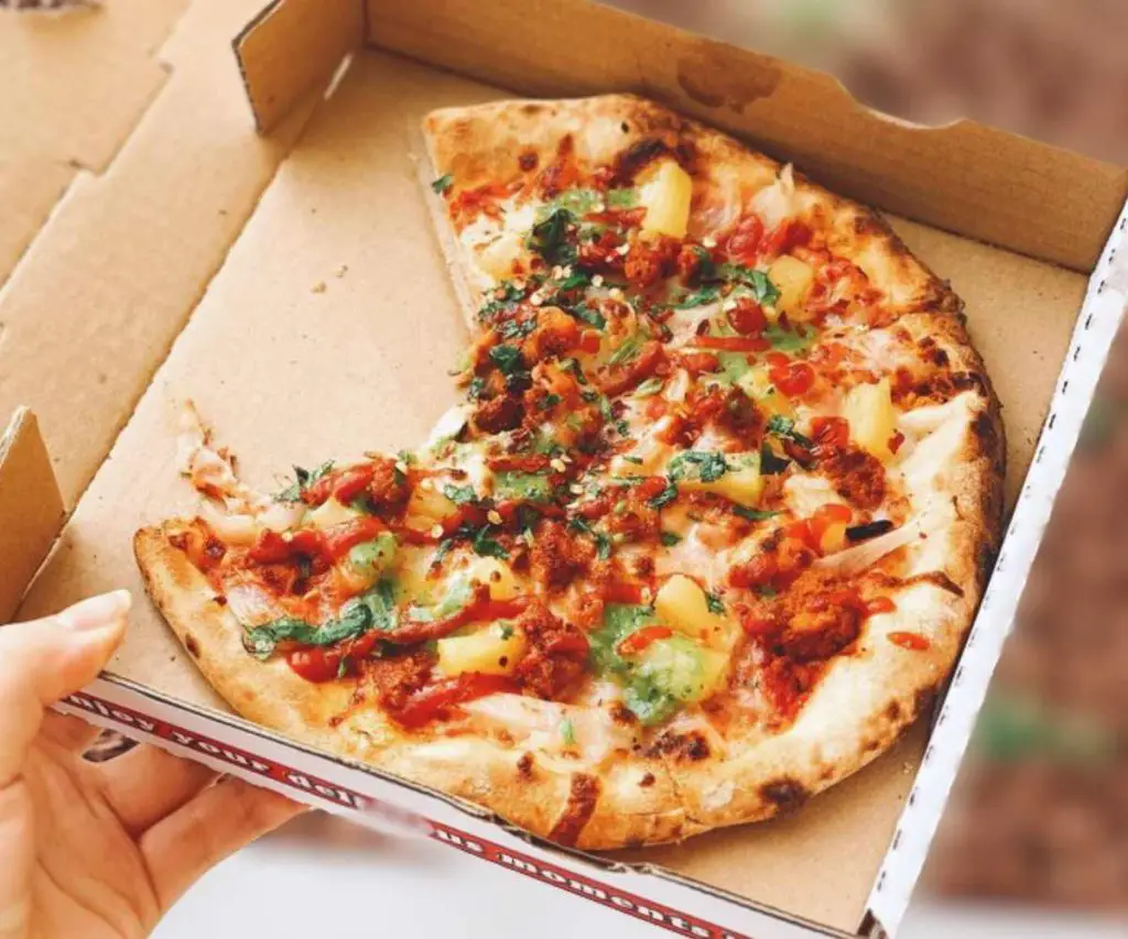 Freshly baked pizza in a cardboard box, topped with cheese, peppers, and fresh herbs, ideal for takeout and delivery, perfect for food lovers seeking delicious destination dining experiences.