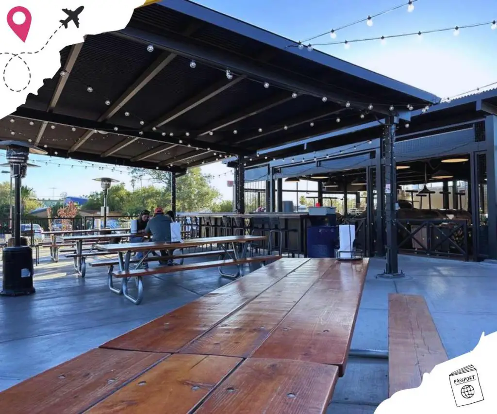 Outdoor dining area with wooden picnic tables, string lights, and a modern rooftop bar at a travel destination.