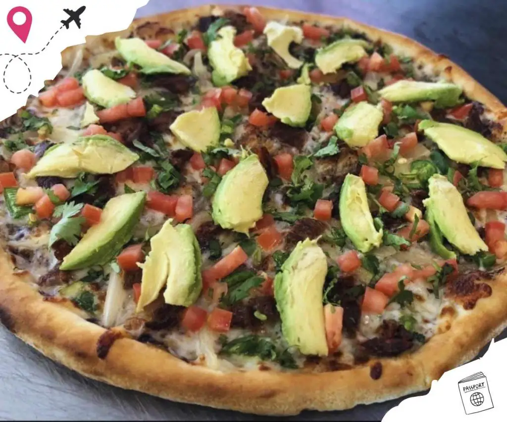 Freshly baked pizza topped with avocado, diced tomatoes, cilantro, and melted cheese, offering a delicious fusion of flavors and textures, perfect for a satisfying meal or snack.