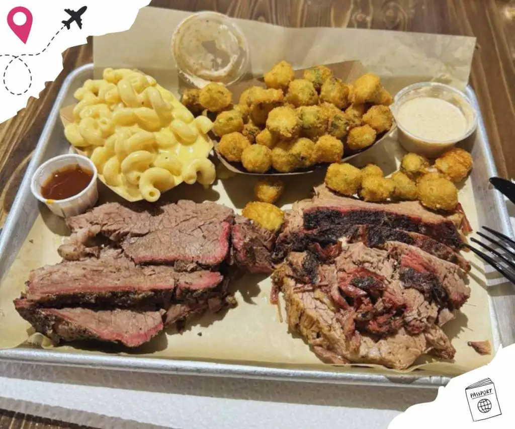 Beef brisket with crispy fried chicken bites, macaroni and cheese, and dipping sauces on a metal tray, served as a hearty American barbecue meal.