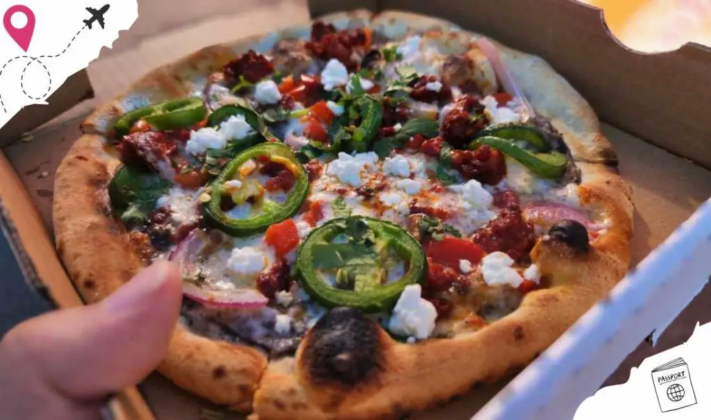 Freshly baked pizza with green peppers, cherry tomatoes, and feta cheese in a pizza box, perfect for travel food or exploring local cuisine.
