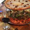 Freshly baked gourmet pizzas with melted cheese, toppings, and crispy crusts served on metal trays with a glass of red wine on a rustic wooden table.