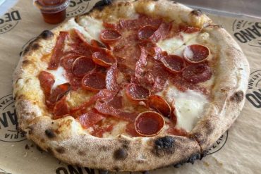 Fresh pepperoni and bacon pizza with a crispy crust served on a branded tray with a side of marinara sauce.