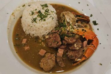 Steamed white rice with seafood stew on white plate, garnished with chopped herbs, served with shrimp, squid, and fish in flavorful broth, delicious coastal cuisine from tropical destination.