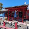 Red coastal cafe with outdoor seating, tropical decor, and vibrant atmosphere, perfect for enjoying local food and drinks in a scenic destination.