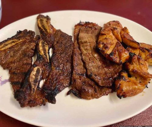 Succulent grilled beef and pork ribs served on a white plate at a restaurant, showcasing delicious barbecue meats perfect for meat lovers and barbecue enthusiasts, traditional grilling style.