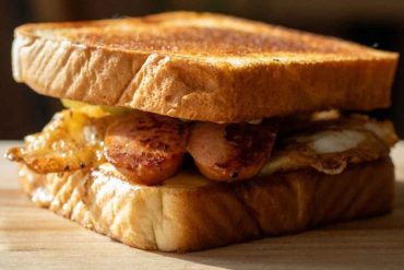 Crispy bacon, fried egg, and sausage sandwich on toasted bread, breakfast, brunch, comfort food, delicious, savory, hearty meal.