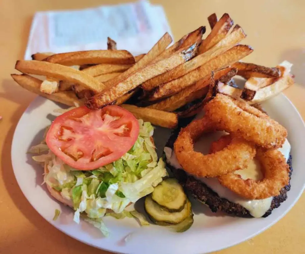 French fries with crispy onion rings, fresh tomato slices, shredded lettuce, and pickles on a white plate, served as a classic American comfort food meal.