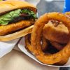 Crispy fish sandwich with fresh lettuce, tomato, and tartar sauce served with golden onion rings for classic American comfort food.