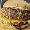 Juicy cheeseburger with crispy fried chicken patty, melted cheddar cheese, and savory beef patty, topped with shredded cheese, served in a toasted bun. Perfect for fast food lovers and burger enthusiasts.