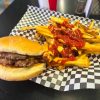 Burger with fries and ketchup on black checkered paper, serving American comfort food at a casual dining restaurant.