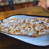 Thin-crust garlic cheese bread pizza served on a black-and-white plate in a cozy restaurant setting. Perfect for sharing, featuring melted cheese, garlic, and crispy bread, ideal for pizza lovers and casual dining.