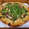 Fresh gourmet pizza with arugula, prosciutto, and balsamic drizzle in a takeout box, showcasing delicious Italian cuisine and perfect for pizza lovers.