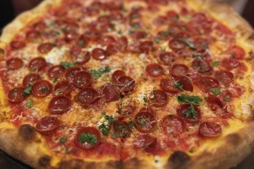 Slices of pepperoni pizza topped with fresh herbs on a pizza oven crust, showcasing a delicious, classic American-style pizza. Perfect for food lovers seeking tasty travel-inspired dining experiences.