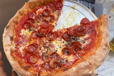 Fresh pepperoni pizza served on a metallic tray at a restaurant, showcasing classic Italian-style pizza with a golden crust, melted cheese, and vibrant tomato sauce. Perfect for pizza lovers and food enthusiasts.
