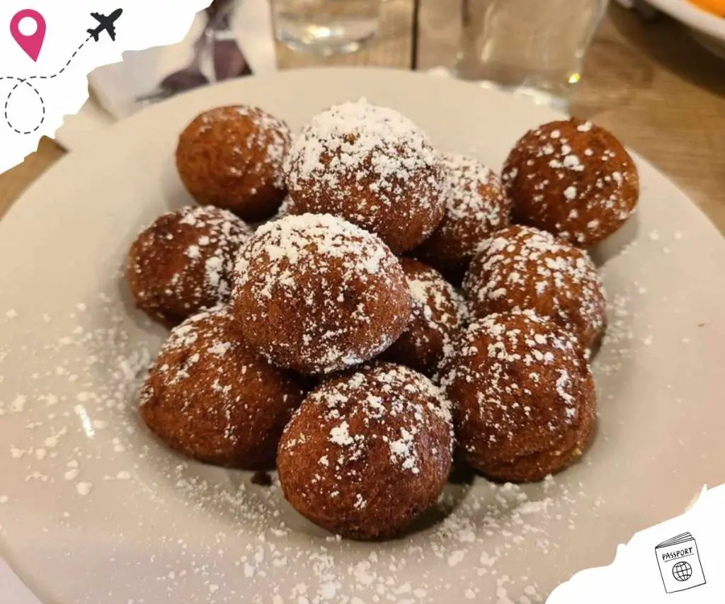 Fried dough balls dusted with powdered sugar, served on a white plate, perfect for dessert or snack in international cuisines.