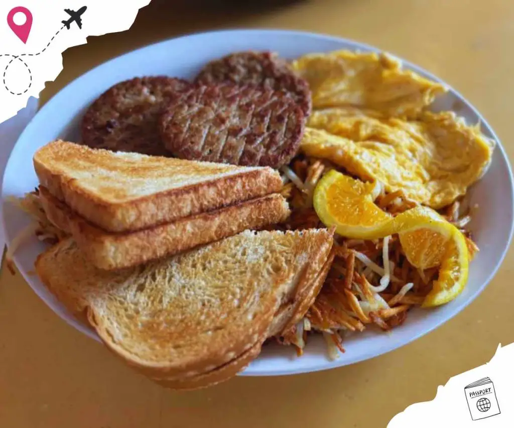 Buttermilk fried chicken breakfast with sausage, toast, and scrambled eggs on a white plate in a cozy restaurant setting.