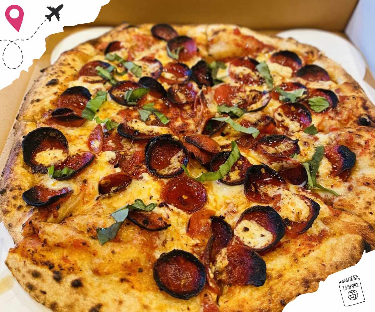 Crispy pepperoni pizza topped with fresh basil and melted cheese in a takeout box.