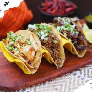 Savory street tacos with shredded chicken, beef, and pork topped with fresh cilantro and onions, served with lime wedges and assorted salsas on a wooden platter.
