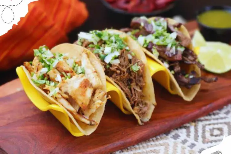 Savory street tacos with shredded chicken, beef, and pork topped with fresh cilantro and onions, served with lime wedges and assorted salsas on a wooden platter.