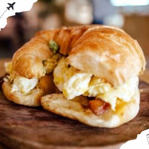Crispy breakfast sandwich with scrambled eggs and bacon on a wooden board.