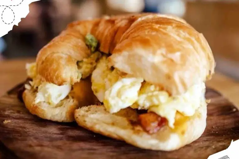 Crispy breakfast sandwich with scrambled eggs and bacon on a wooden board.