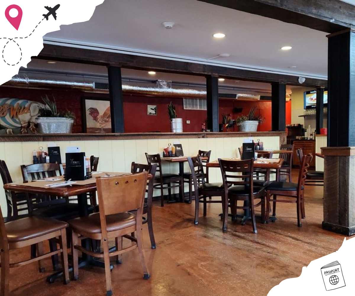 Modern restaurant interior with wooden tables and chairs, decorated with plants and artwork, offering a cozy dining atmosphere suitable for travelers and locals alike.