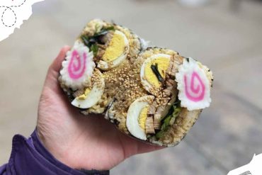 Sushi roll with boiled eggs, green herbs, and sesame seeds held in hand, representing Japanese cuisine and travel food experiences.